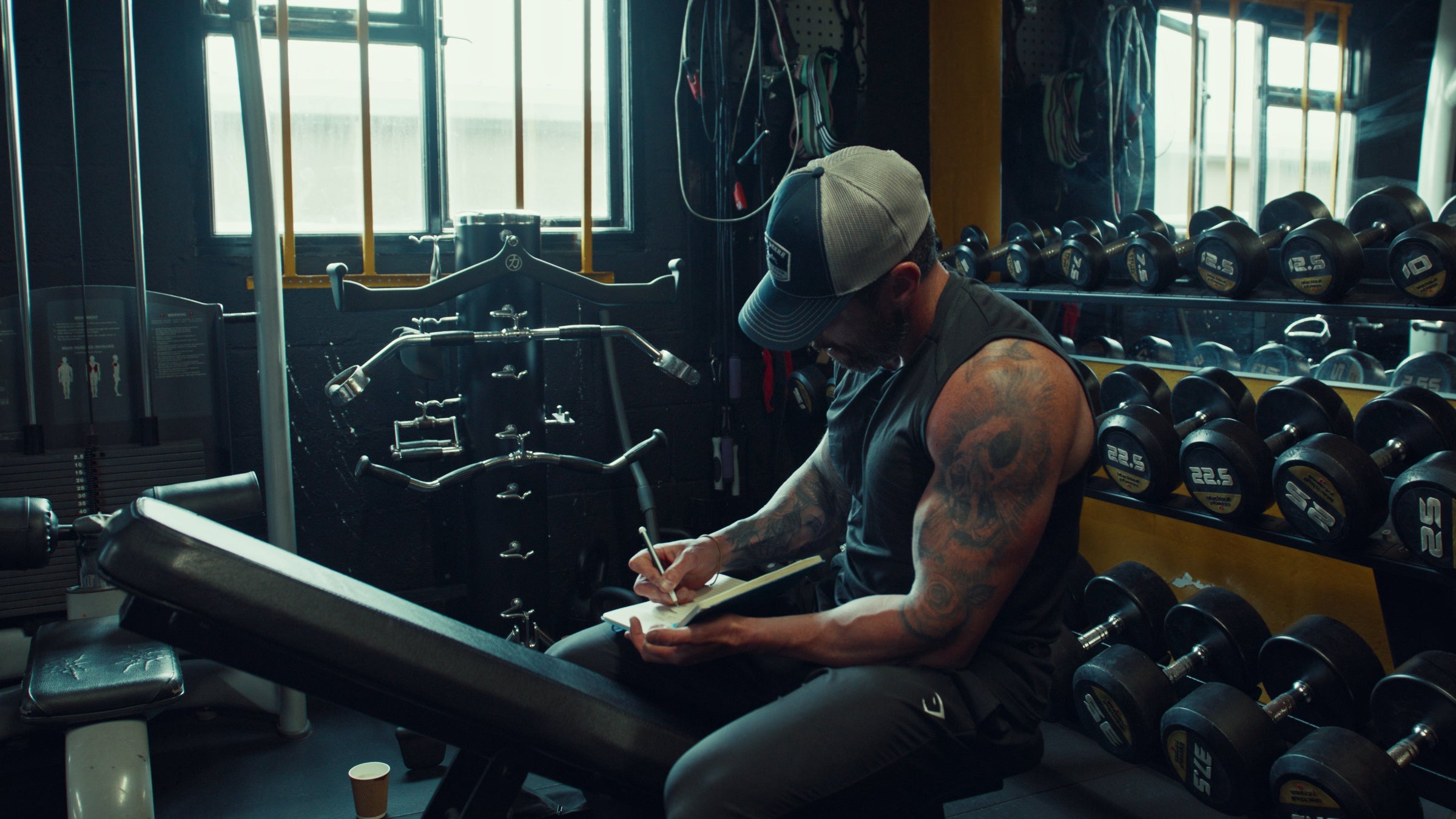 Jonny Collins writing on a piece of paper in a gym setting with weights and exercise equipment around